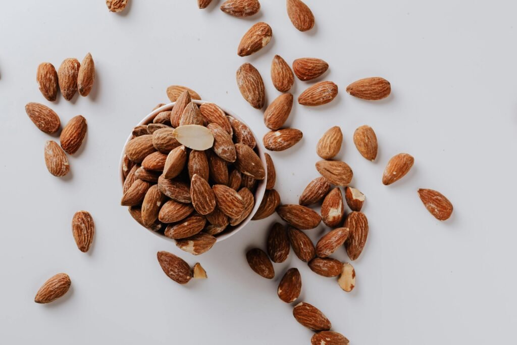 Healthy raw almonds scattered around a bowl on a white surface, showcasing a top view arrangement.